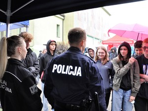 przed młodzieżą stoi policjant, chłopiec ma założone kajdanki, uśmiecha się