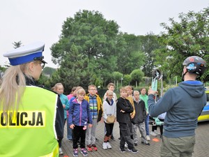 policjantka i ksiądz rozmawiają z młodzieżą, ksiądz trzyma w ręku hulajnogę