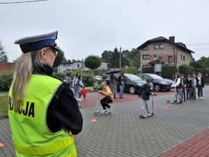 policjantka obserwuje ćwiczenia dzieci na hulajnogach