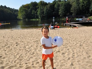 na plaży stoi dziewczynka, w ręce ma piłkę