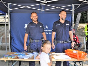 policjanci stoją przed namiotem profilaktycznym, przed nimi stoi dziewczynka