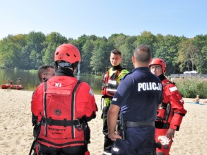 policjant rozmawia ze stojącymi obok niego strażakami