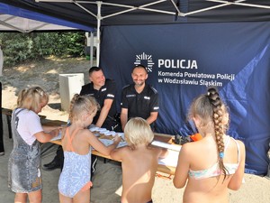 dzieci kolorują kolorowanki, na przeciwko nich siedzą policjanci