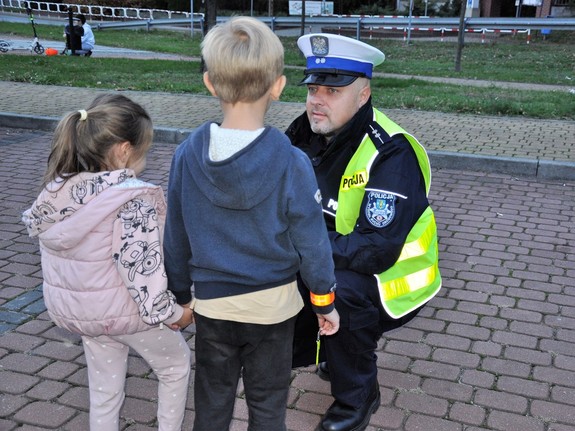 policjant kuca przed dwójką dzieci, rozmawia z nimi