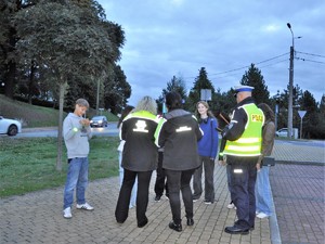 policjant i pracownicy wodzisławskiego starostwa rozmawiają z grupą młodzieży i rozdają im odblaski