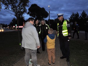 policjant rozmawia z uczestnikami akcji profilaktycznej zachęcającej do noszenia odblasków