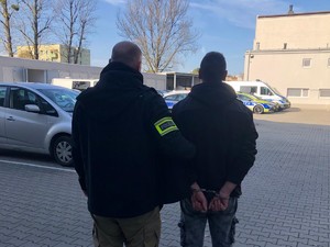 policjant trzyma za ramię zatrzymanego mężczyznę, stoją tyłem