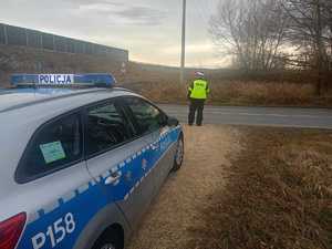 policjant obserwuje ruch pojazdów, stoi przy drodze