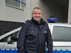 na zdjęciu obok radiowozu stoi policjant dzielnicowy