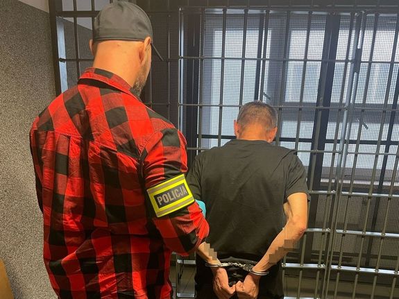 nieumundurowany policjant stoi obok zatrzymanego mężczyzny, stoją tyłem do zdjęcia