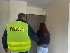 policjant trzyma zatrzymaną kobietę, stoją tyłem do zdjęcia