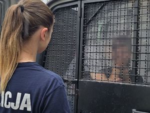 w radiowozie znajduje się zatrzymany mężczyzna, przed radiowozem stoi policjantka