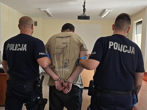 zatrzymanego mężczyznę trzymają policjanci. Wszyscy stoją tyłem do zdjęcia