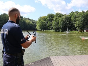 policjant zdalnie steruje pływającym po zbiorniku wodnym sprzętem ratowniczym