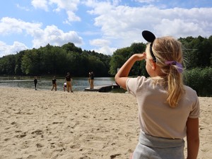dziewczynka stoi na plaży, obserwuje strażaków stojących przy brzegu zbiornika wodnego