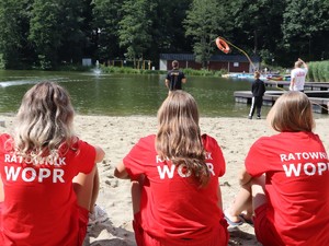 na plaży tyłem do zdjęcia siedzą trzy ratowniczki wodne