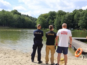 na brzegu zbiornika wodnego stoi policjant, strażak i ratownik wodny