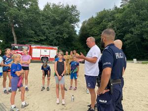 policjant i ratownik wodny prowadzą spotkanie profilaktyczne na plaży