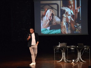 prelegent przemawia ze sceny, w tle widać prezentację przedstawiającą zdjęcia dzieci