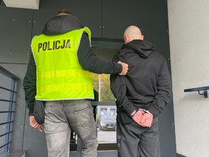 policjant trzyma zatrzymanego mężczyznę, obaj stoją tyłem do zdjęcia