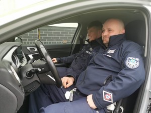 na zdjęciu widać siedzących w radiowozie dwóch policjantów